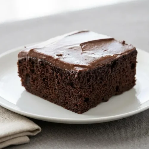 Chocolate keto cake with smooth, glossy chocolate frosting, baked in a square glass dish and cut into nine servings.