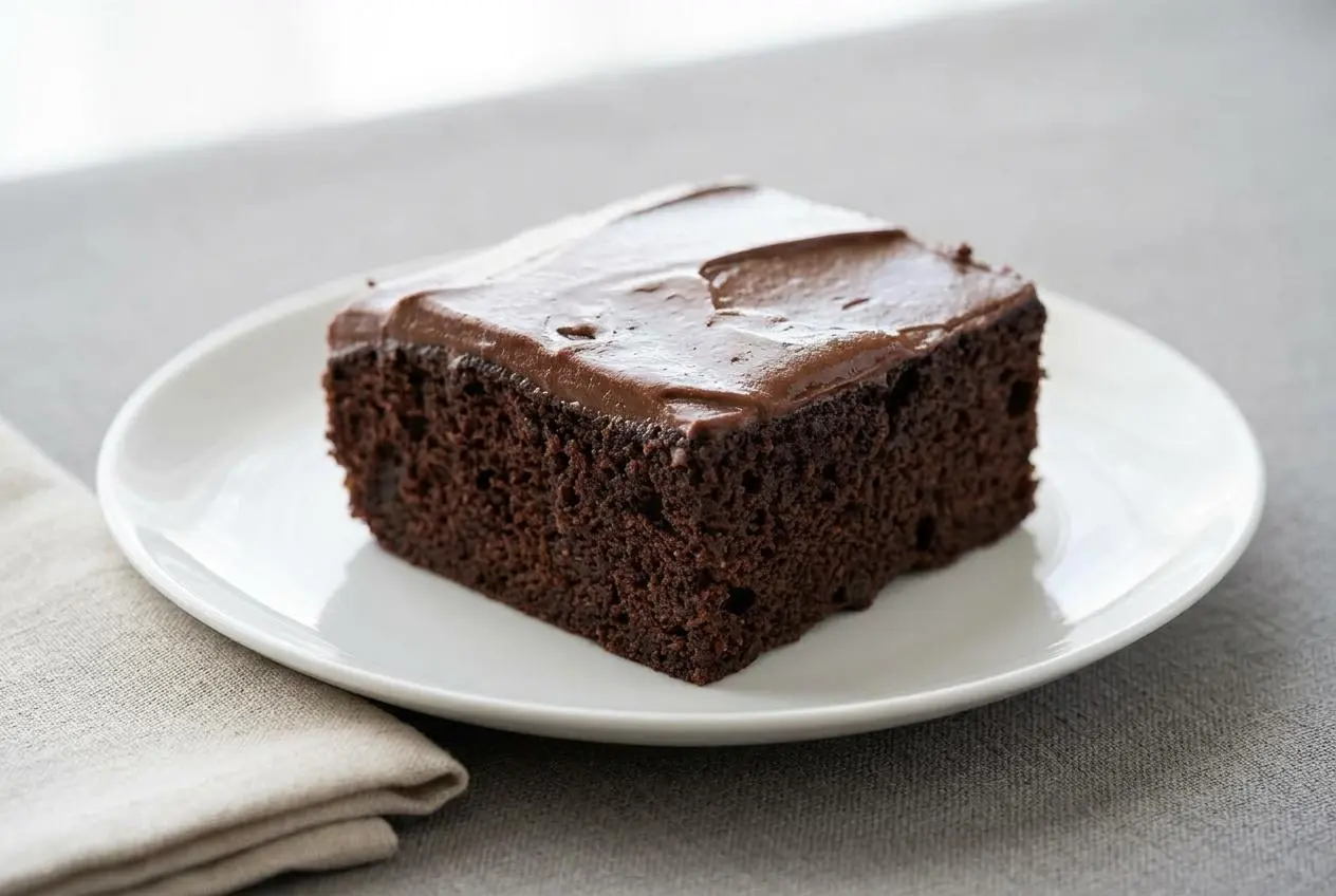 Chocolate keto cake with smooth, glossy chocolate frosting, baked in a square glass dish and cut into nine servings.