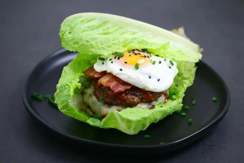 A keto breakfast burger stacked in a crisp lettuce wrap with a juicy beef patty, melted swiss cheese, bacon, and a fried egg.