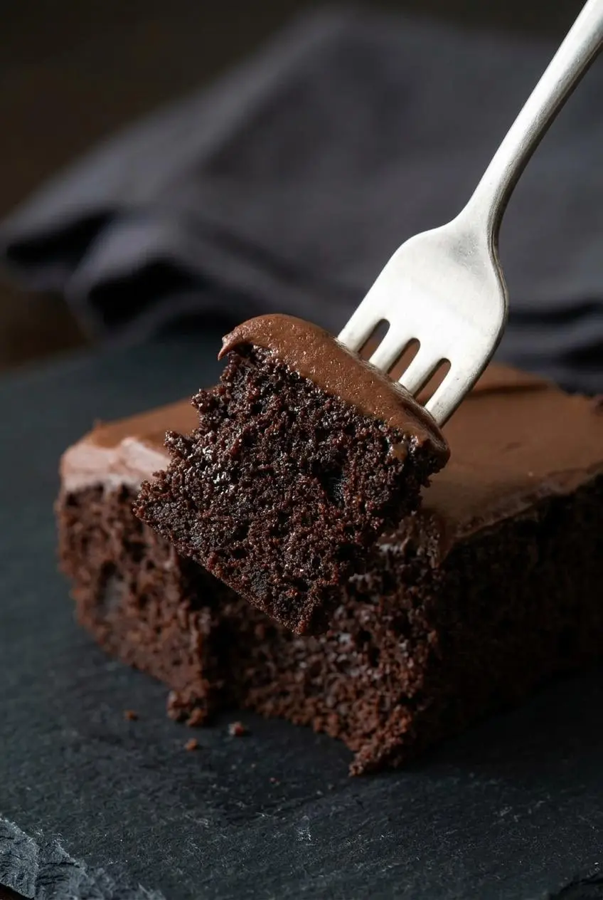 Extreme close-up of a fork lifting a piece of chocolate cake, showing the moist, fudgy crumb and glossy frosting.