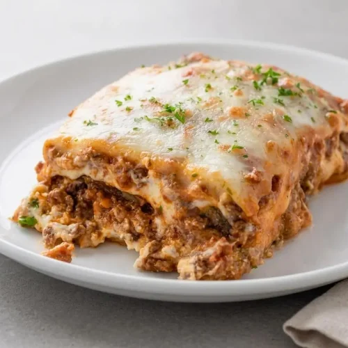 Keto eggplant lasagna in a white baking dish with a slice removed, showing layers of meat sauce, ricotta, and a golden mozzarella topping.
