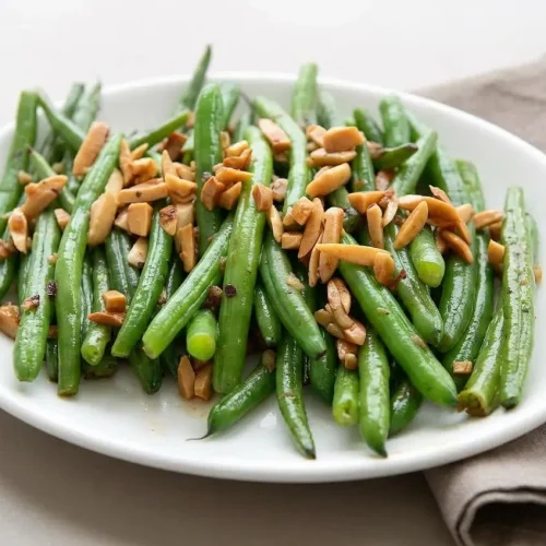 Keto Green Beans Almondine in a white serving dish, glistening with butter and topped with golden toasted slivered almonds.