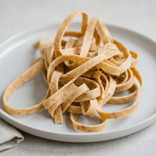 A ceramic bowl of homemade keto pasta ribbons tossed in a creamy mushroom sauce, showing the soft, pliable texture of the noodles.
