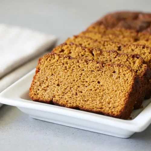 A whole loaf of Keto Pumpkin Bread with a golden-brown baked top, resting on parchment paper after cooling.