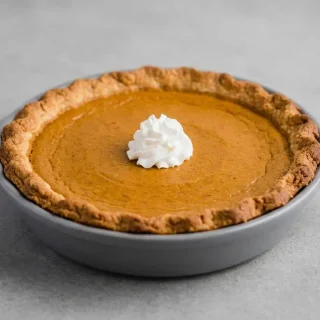 A whole keto pumpkin pie with a flaky almond flour crust and creamy orange filling, with one slice removed to show the texture.