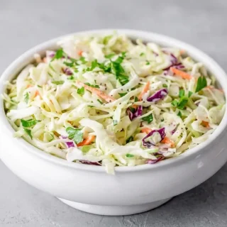 A bowl of fresh keto coleslaw recipe featuring shredded green and purple cabbage tossed in a creamy, glossy dressing.