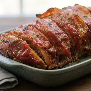 Low carb meatloaf topped with crispy bacon and a glossy caramelized glaze in a baking dish.