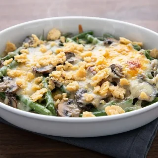 Creamy keto green bean casserole with bubbly melted cheese, golden Parmesan crisp topping, and mushrooms in a baking dish.