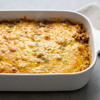Baked keto taco casserole in a ceramic dish with a bubbling, golden-brown melted cheddar cheese topping.