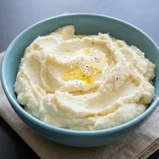 Creamy keto mashed cauliflower recipe whipped with sharp cheddar cheese and butter in a serving bowl.