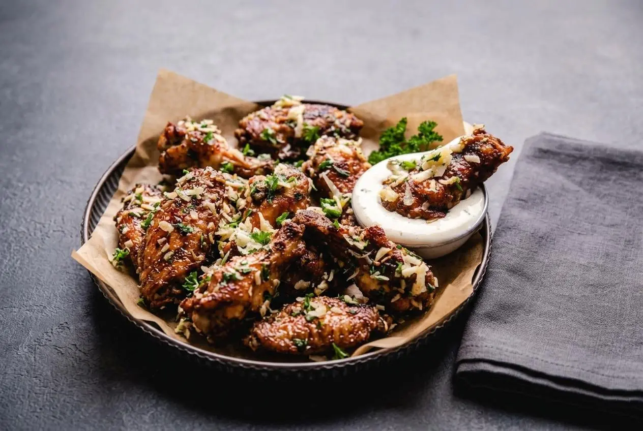 Platter of crispy golden keto chicken wings recipe tossed in garlic parmesan sauce and fresh herbs.