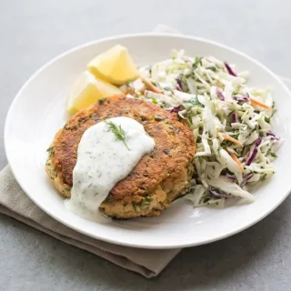 Crispy keto salmon patties with a golden crust and tender center garnished with fresh green herbs.