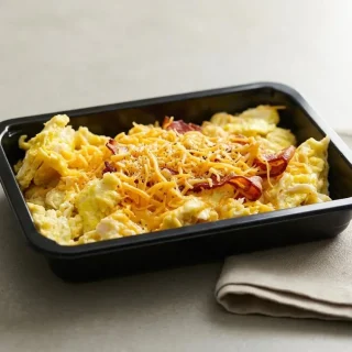 A finished plate of this easy keto scrambled eggs recipe served with crispy bacon and melted cheddar.
