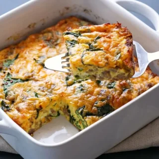 Freshly baked keto breakfast casserole with a golden cheddar cheese crust, savory sausage, and wilted spinach.