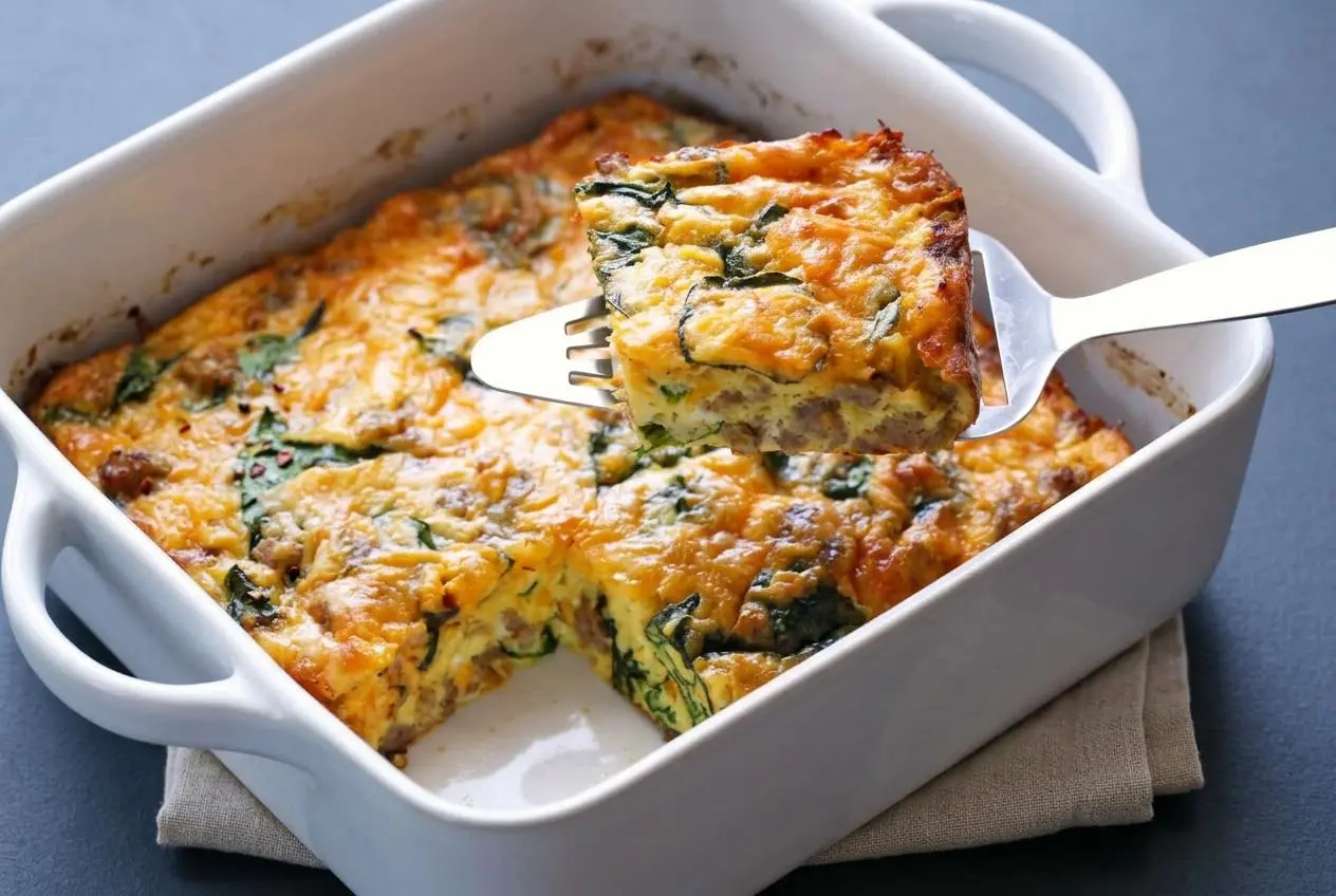 Freshly baked keto breakfast casserole with a golden cheddar cheese crust, savory sausage, and wilted spinach.