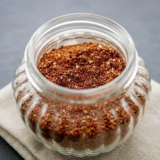 A small glass jar filled with vibrant brick-red keto taco seasoning recipe blend, showing a fine and uniform texture.