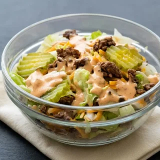 Keto big mac salad recipe featuring crisp lettuce topped with browned ground beef, cheddar cheese, and a creamy special sauce.