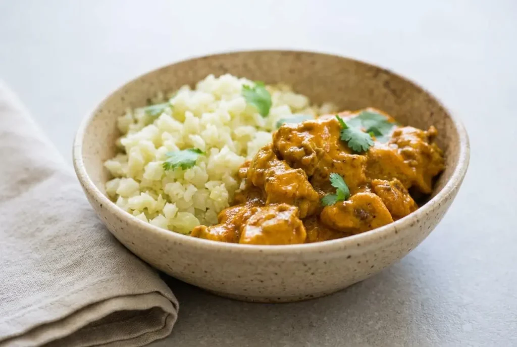 A skillet of creamy keto butter chicken recipe with tender chicken in a glossy, rich orange-gold tomato cream sauce.