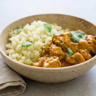 A skillet of creamy keto butter chicken recipe with tender chicken in a glossy, rich orange-gold tomato cream sauce.
