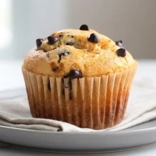Golden domed keto chocolate chip muffins with melted sugar-free chocolate pockets baked in paper liners.