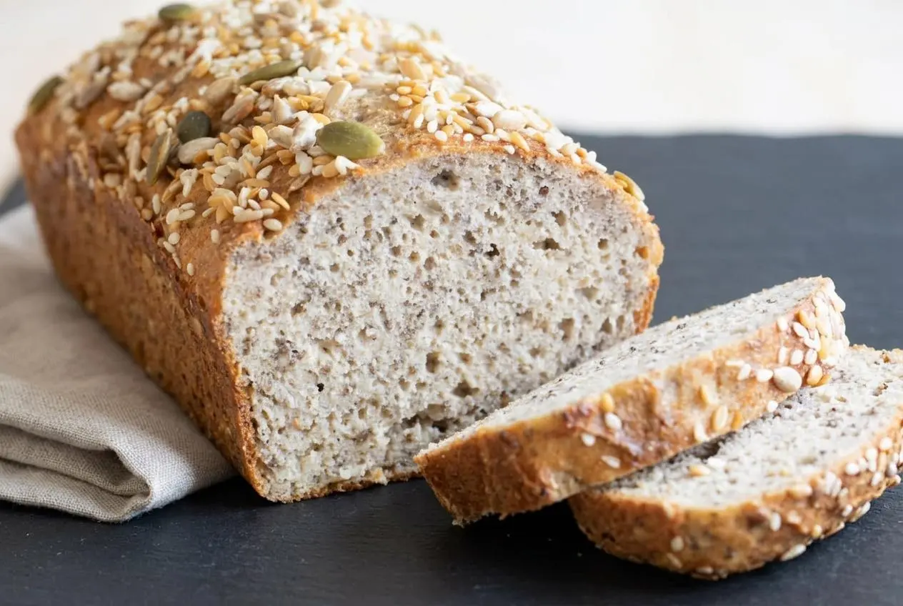 Slice of freshly baked keto cottage cheese bread with a golden-brown seed crust and soft, springy interior.