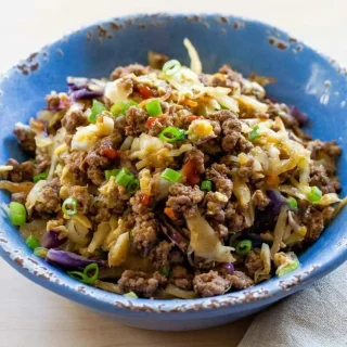 Keto egg roll in a bowl in a skillet with savory beef, tender cabbage, and a glossy drizzle of sesame oil.