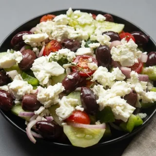 Keto greek salad in a bowl with crisp cucumbers, cherry tomatoes, Kalamata olives, and glossy olive oil dressing.