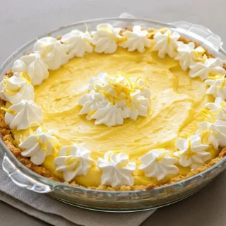 Slice of keto lemon pie with a creamy yellow filling, toasted coconut crust, and a whipped cream dollop.
