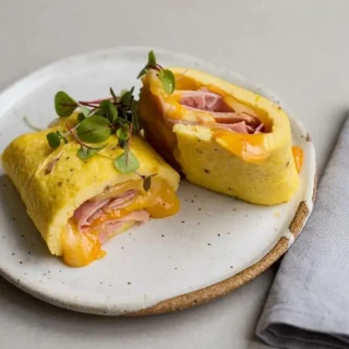 Finished keto omelette sliced into tender rolls with melted Swiss cheese and shaved ham.