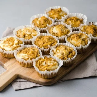 Keto pumpkin cream cheese muffins with a golden spiced crumb and silky cheesecake swirl on top.