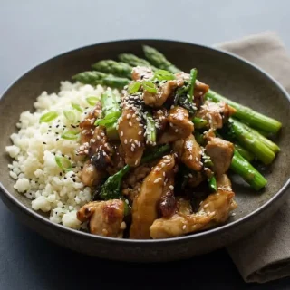 Glistening keto teriyaki chicken thighs with bright green broccolini and sesame seeds over cauliflower rice.
