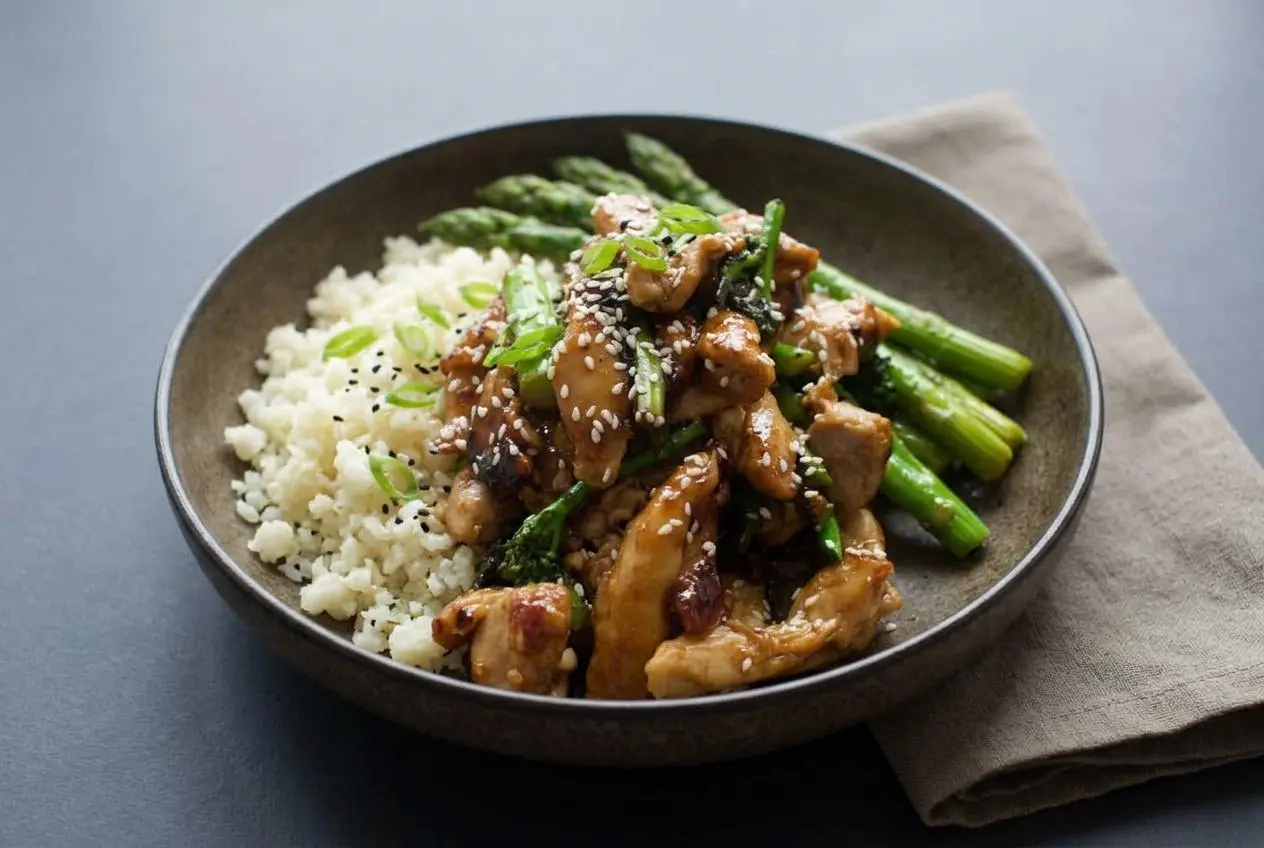 Glistening keto teriyaki chicken thighs with bright green broccolini and sesame seeds over cauliflower rice.