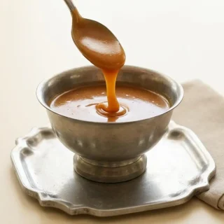 Glossy golden keto caramel sauce pooled beautifully in a glass jar, showing a smooth and velvety texture.