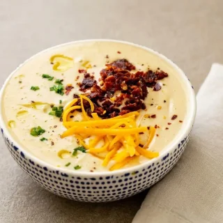 Velvety keto cauliflower soup in a bowl garnished with crispy bacon and fresh chives.