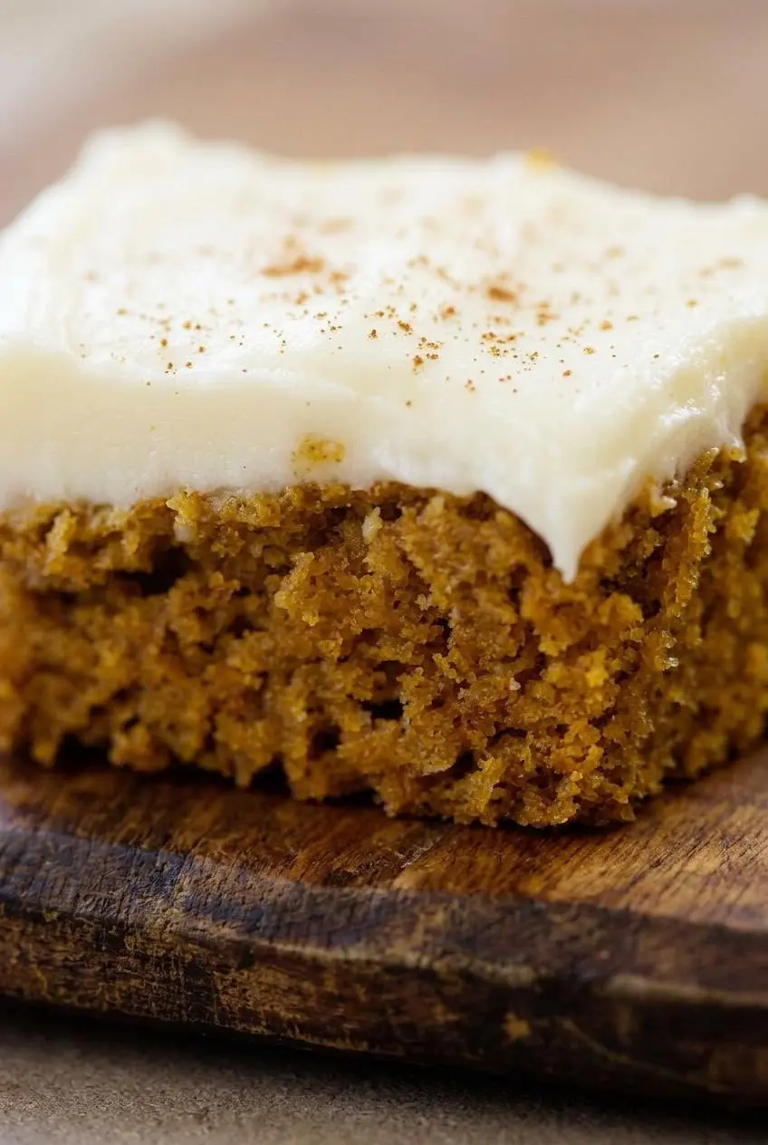 Macro close-up of fluffy cream cheese frosting swirls over a moist almond flour pumpkin bar.