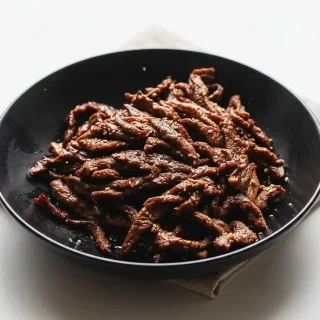 Keto beef bulgogi with caramelized edges and a glossy savory glaze garnished with toasted sesame seeds.