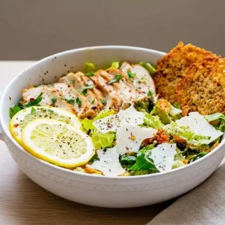 Keto caesar salad recipe topped with sliced grilled chicken and golden crisp parmesan croutons.