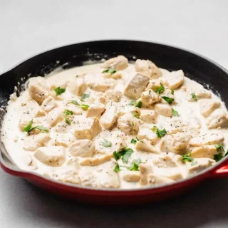 Keto chicken alfredo in a skillet with golden seared chicken breast and glossy garlic parmesan cream sauce.