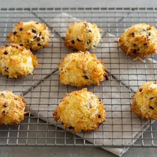 Keto coconut cookies with toasted golden edges and melted dark chocolate chips on a baking sheet.