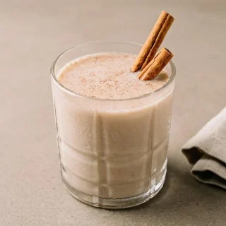Chilled keto coquito recipe poured into a glass with a creamy, lightly frothy top and a dusting of cinnamon.
