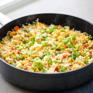Savory keto fried rice with cauliflower grains, soft egg ribbons, diced bell peppers, and a glossy sesame finish.