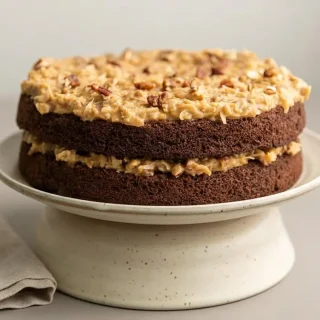 Keto german chocolate cake with rich coconut-pecan frosting between tender dark chocolate layers.