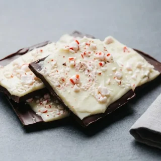 Keto peppermint bark broken into layered pieces with dark and white chocolate on a parchment sheet.