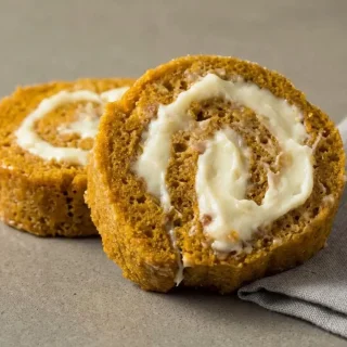 Keto pumpkin roll recipe showing a sliced spiced sponge roulade filled with pillowy whipped cream.