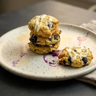Glazed keto blueberry cookies with a tender buttery crumb and bursting whole fruit on a cooling rack.