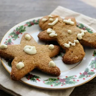 Keto gingerbread cookies decorated with delicate cream cheese icing showing crisp golden edges.