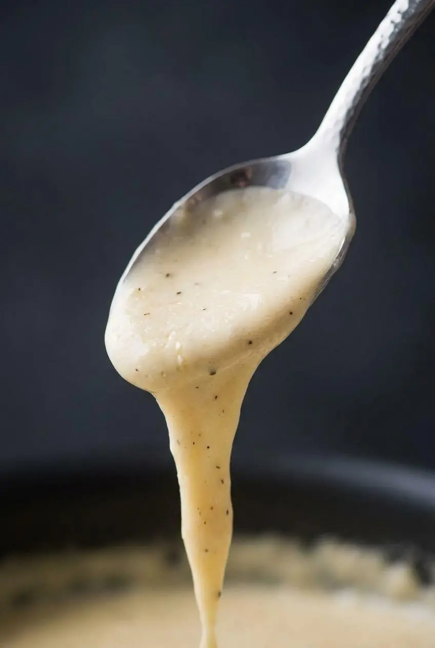 Metal spoon lifting velvety keto alfredo sauce to test the smooth, cohesive coating texture.