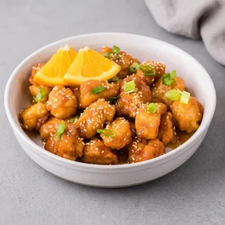 Keto orange chicken bites coated in glossy citrus glaze in a serving bowl