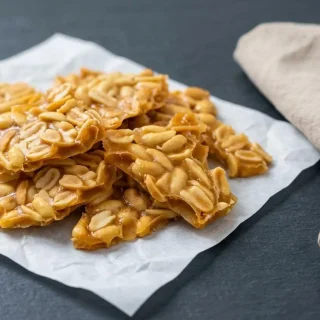 Crisp keto peanut brittle broken into golden shards with roasted salted peanuts and a glossy amber caramel finish.