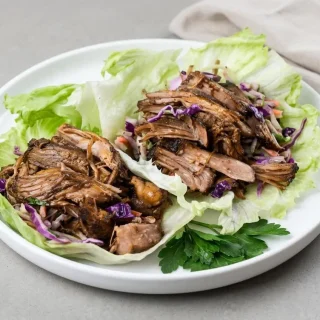 Tender keto pulled pork recipe shreds with a glossy spiced finish in crisp lettuce leaves.